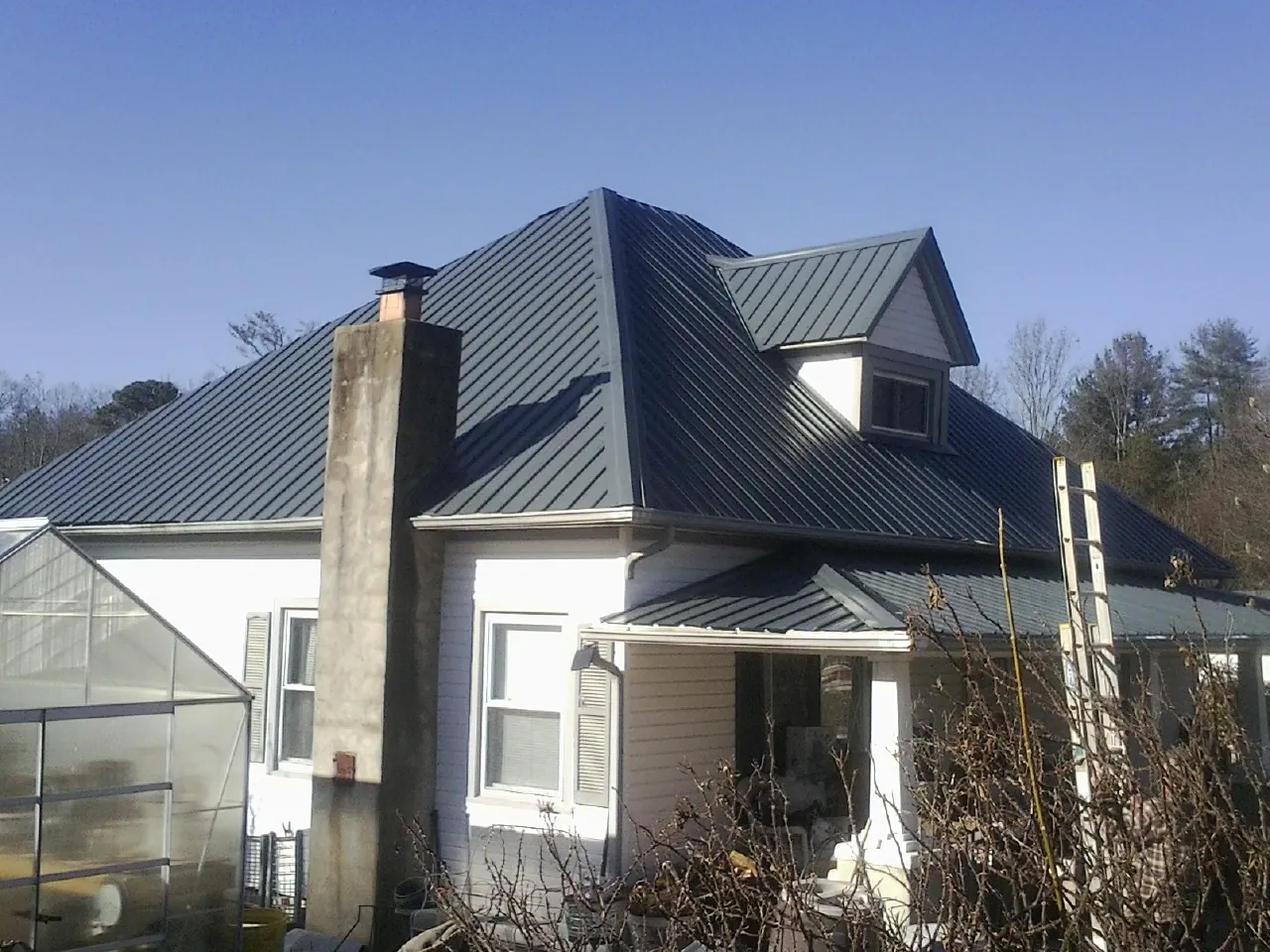 Dark blue standing seam metal roof on a white farmhouse with dormer — Slate & Tile Roof Repair by Roofing Brothers in Fort Loudon