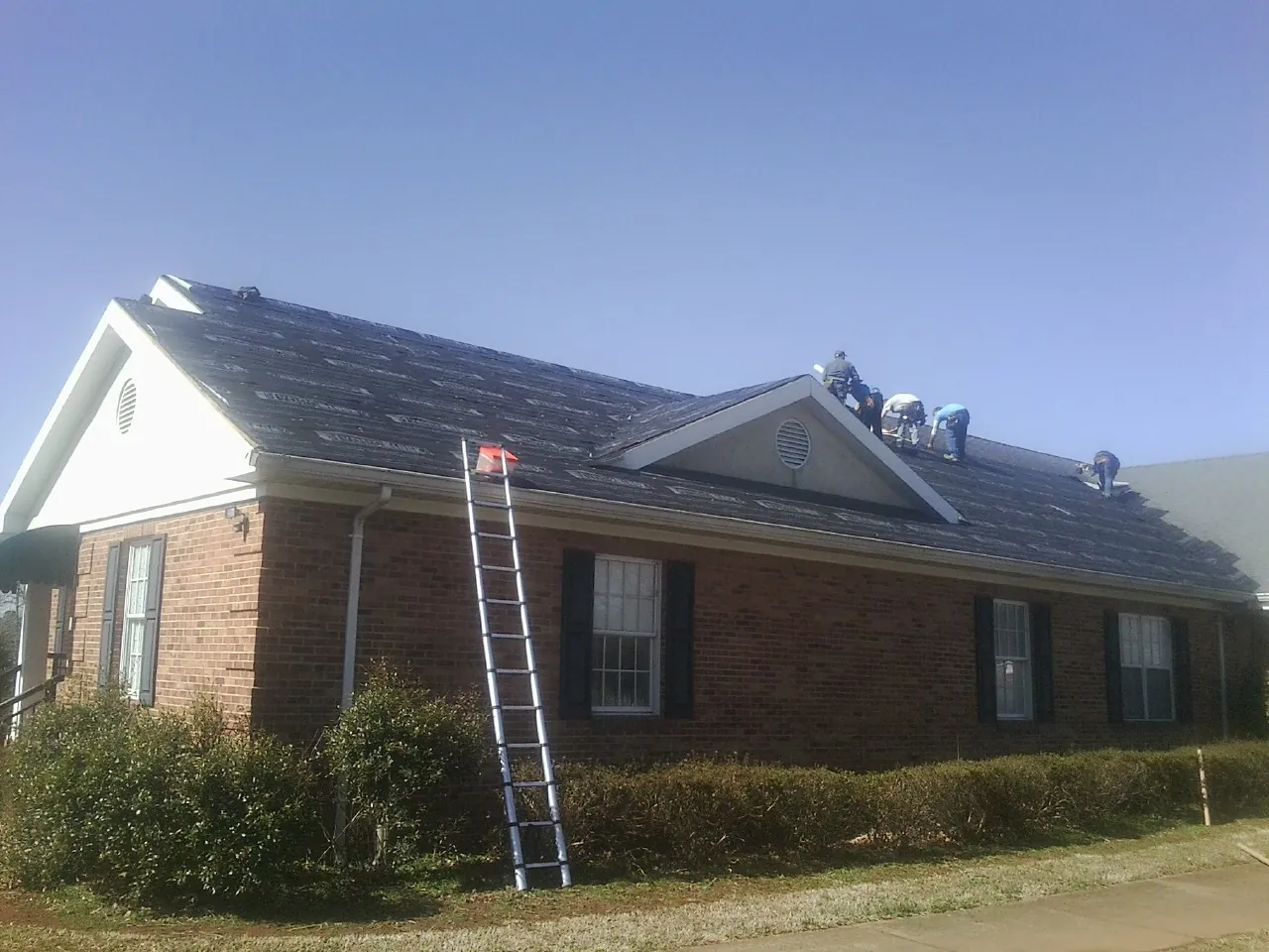 Crew tearing shingles off a brick ranch roof with a ladder set — Emergency Roof Repair work by our crew in Fort Loudon