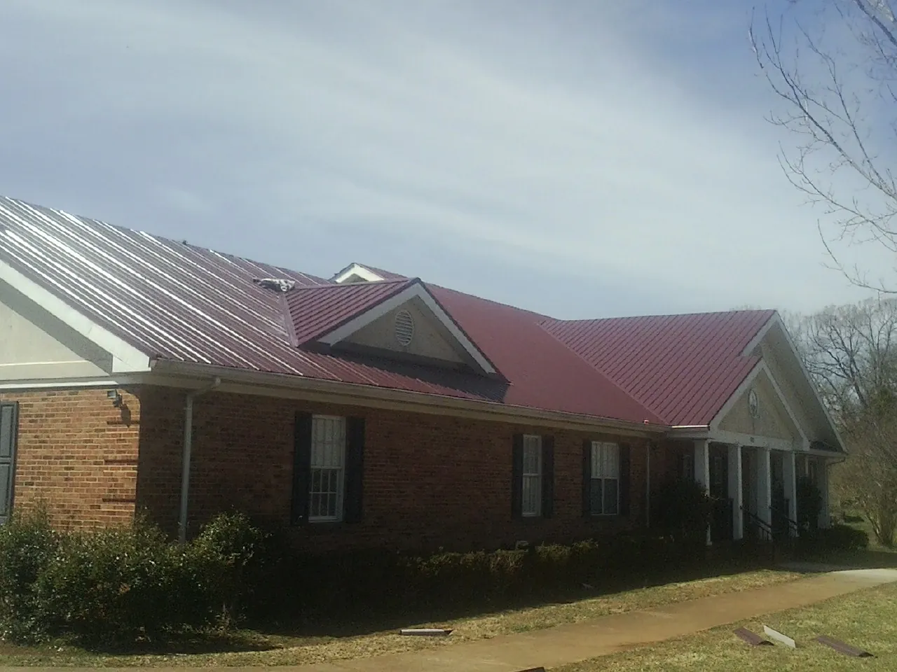 Red metal roof with gabled entries on a long brick building, from a Hail Damage Roof Repair job in Fort Loudon