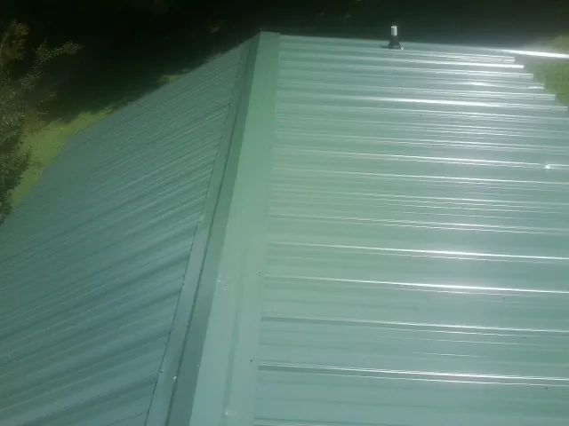 New green metal panels meeting at the ridge of a roof — Flat Roof Repair work by our crew in Fort Loudon