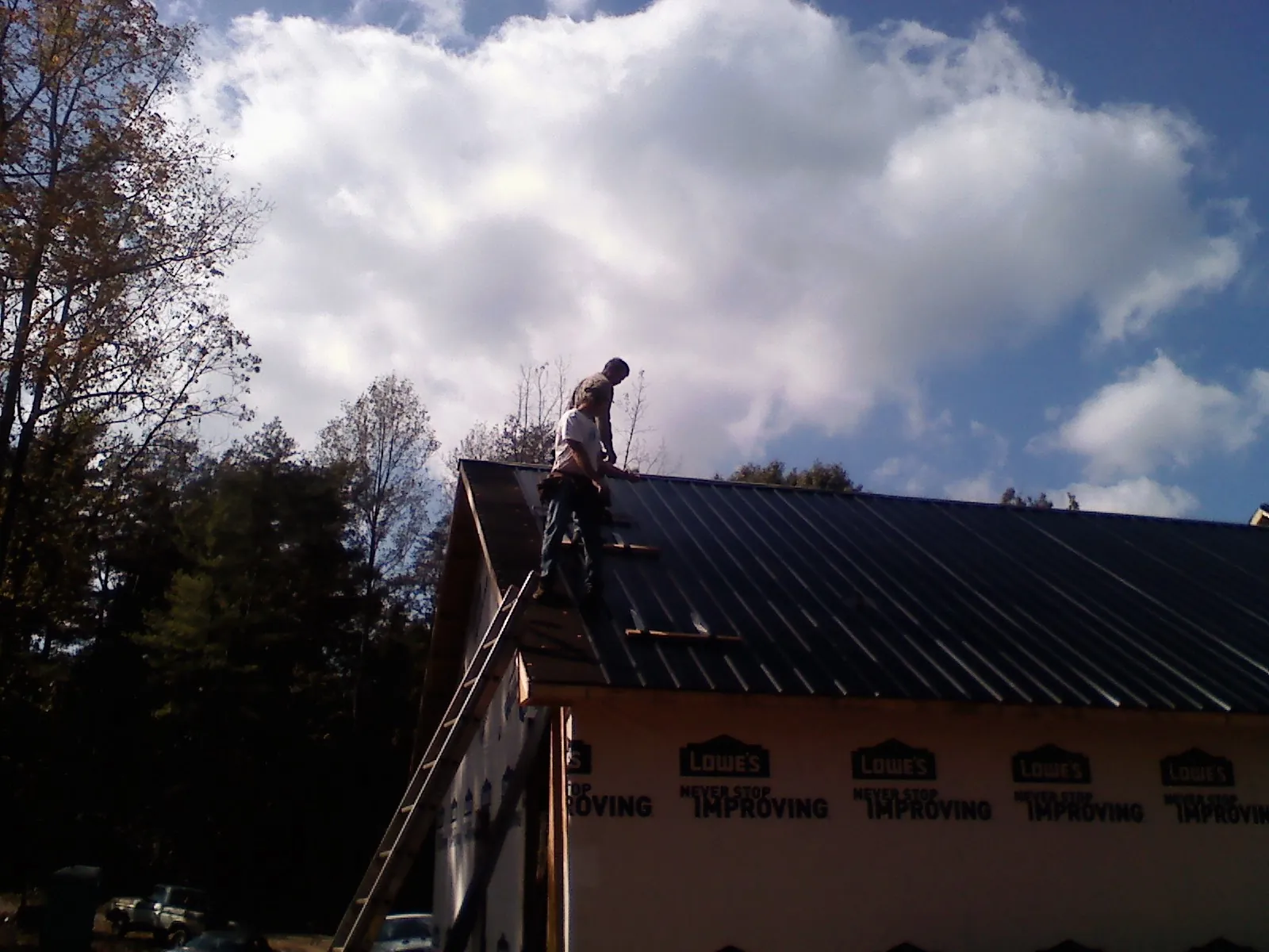 Roofer fastening dark metal panels high against a cloudy sky, from a Roof Inspection job in Fort Loudon