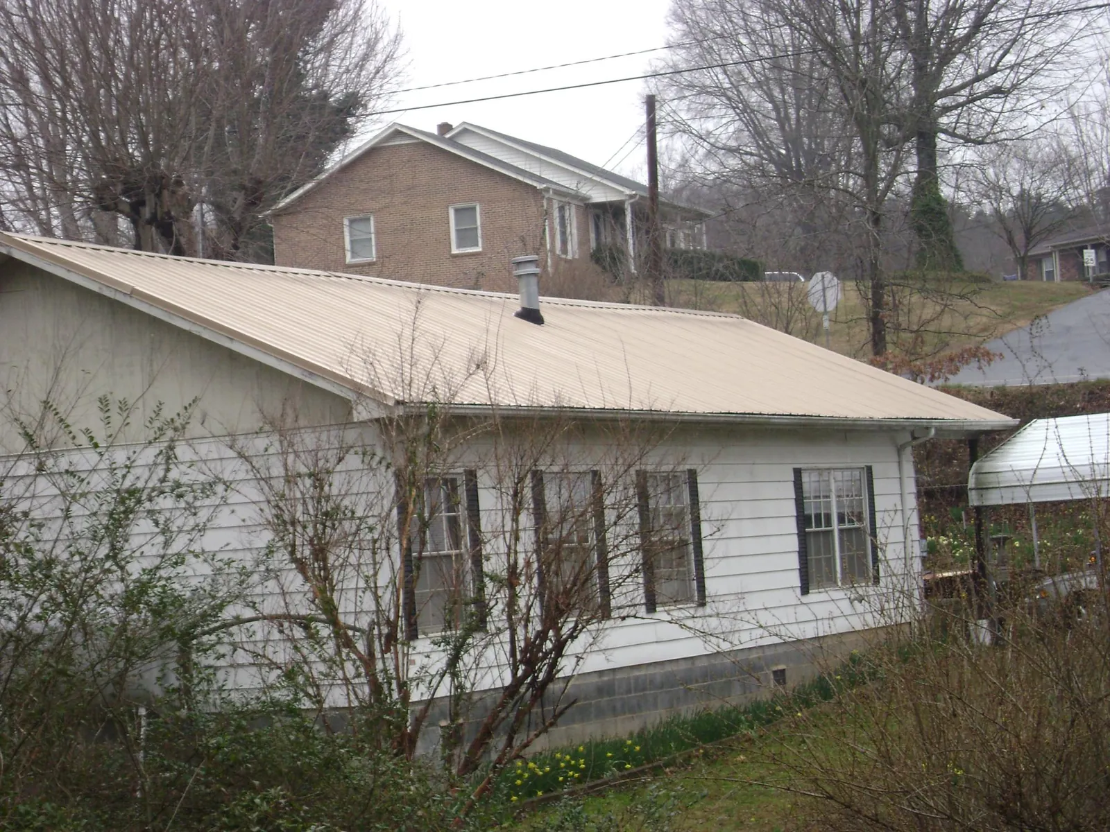 Tan metal roof on a white sided house set into a hillside — Commercial Roofing by Roofing Brothers in Fort Loudon