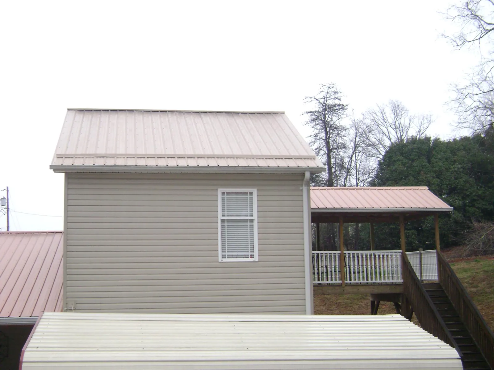 Tan metal roofs on a two story addition and attached porch, from a Roof Replacement job in Fort Loudon